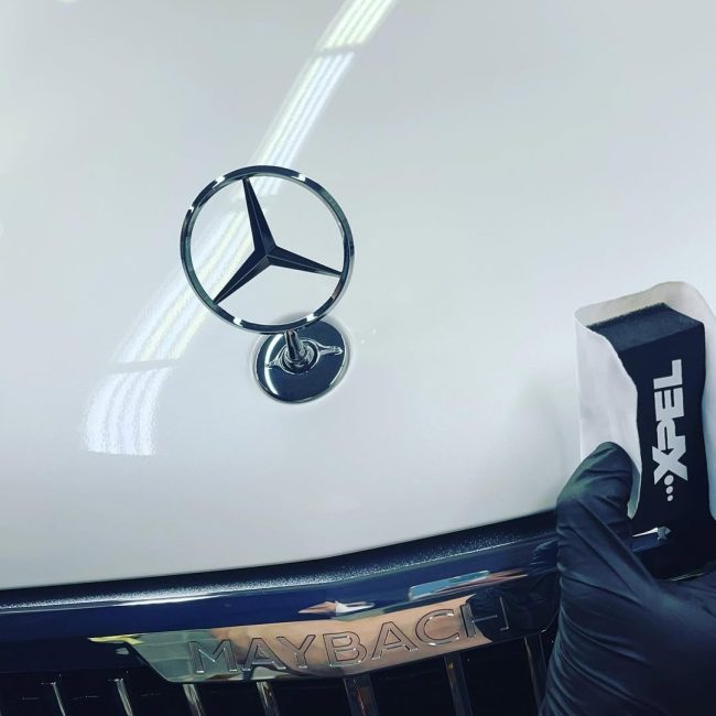 Close-up of XPEL paint protection film being applied to the hood of a white Mercedes-Maybach, showcasing high-end detailing precision