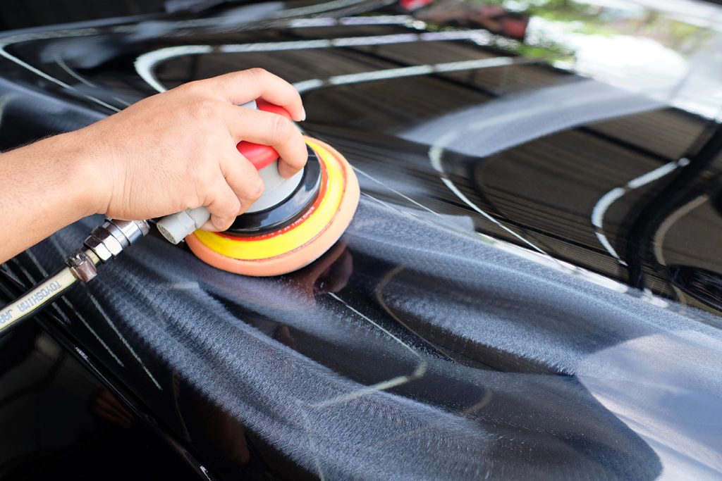 Close-up of a technician performing paint correction on a glossy black supercar using a dual-action polisher