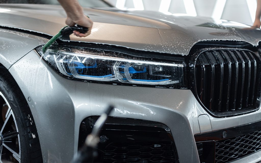 Close-up of a silver BMW with partial paint protection film (PPF) being installed on the hood and headlights during the detailing process