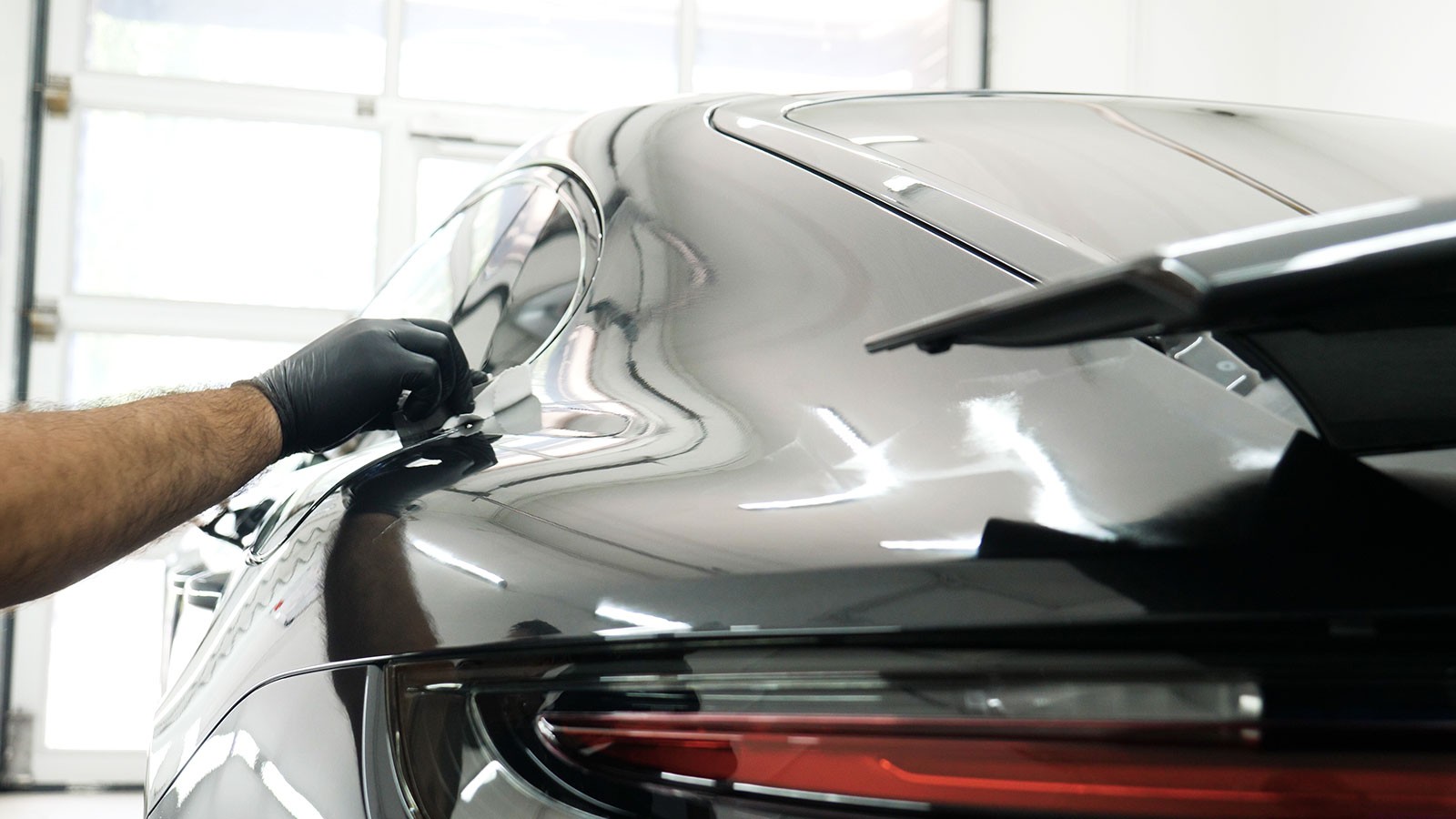 Technician applying ceramic coating on the rear quarter panel of a black Porsche for high-gloss protection and hydrophobic finish
