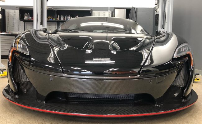 Gloss black McLaren with full front paint protection film installed, reflecting workshop lighting in a high-end detailing studio