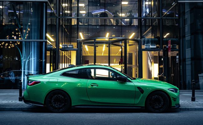 Striking green BMW M4 coupe protected with full body paint protection film (PPF), parked in front of a modern glass building at night under city lights